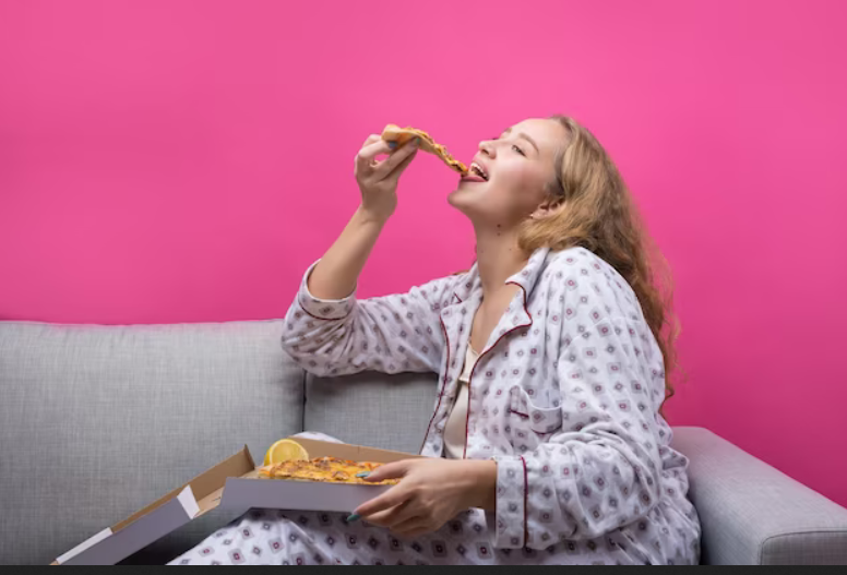 Дівчина сидить на дивані і їсть піцу